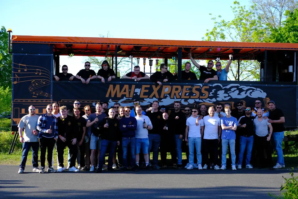 Die Crew des Mai Express steht vor dem orangefarbenen Wagen