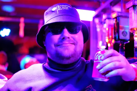Ein Gast mit Hut und Getränk im bunten Licht