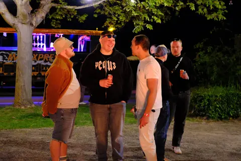 Gäste stehen nachts unter Bäumen am Wagen